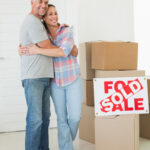Happy couple standing and hugging beside sold sign in their new home